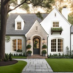 a white house with black doors and windows in the front yard is surrounded by trees