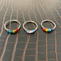 three pairs of hoop earrings with multicolored beads on them sitting on a leather surface