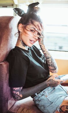 a woman sitting in a chair with tattoos on her arms