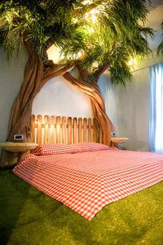 a bed with a red and white checkered bedspread under a large tree