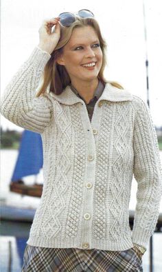 a woman in a white sweater and plaid pants smiles while holding her hat up to her head