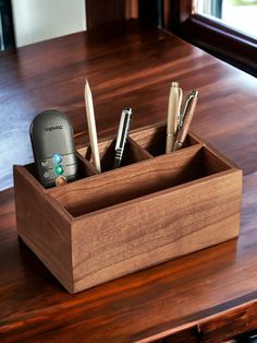 a wooden pen holder with three pens and a cell phone in it on a table