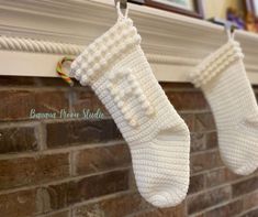 two white knitted stockings hanging from a hook on a fireplace mantel above a brick wall