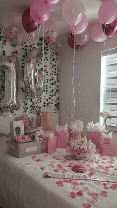 a table topped with lots of pink and white balloons next to a wall covered in confetti