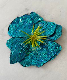 a blue flower with green stems in the center on a white surface, surrounded by sequins