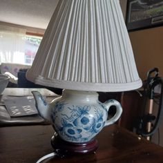 a blue and white teapot shaped lamp on top of a wooden table next to a laptop