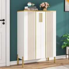 a white and gold cabinet in a room with blue walls, potted plant and books on top