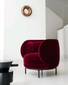 a red chair sitting on top of a white floor next to a black and gold clock