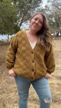 a woman standing on top of a dirt field wearing a brown sweater and ripped jeans