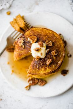 a white plate topped with pancakes covered in butter and pecans next to a fork