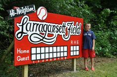 a young boy standing in front of a large sign with baseballs and words on it