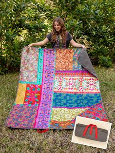 a woman is sitting on the ground with a quilt in front of her and an item next to it