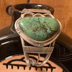 Another vintage piece, this one with a beautiful green stone. The design on this cuff is unique.   There is a small break on the twisted piece in the middle of the band, but it is on the under side and does not affect the design, nor does it bother you while wearing.    On the back of the stone on the silver, there is a signature stracthed in it, we are not sure if it is the artist signature or previous owner. As expected on a well loved piece of jewelry, there are some small stratches on the ba Unique Green Patina Cuff Bracelet, Adjustable Vintage Turquoise Cuff Bracelet, Vintage Multi-strand Turquoise Jewelry, Under Side, Vintage Turquoise Hand-tooled Bracelets, Vintage Nickel-free Turquoise Cuff Bracelet, Artist Signature, Artist Signatures, Green Turquoise