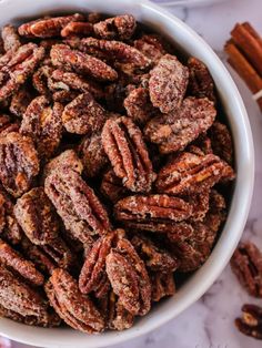 a white bowl filled with pecans next to cinnamon sticks