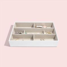 a white box with several compartments filled with jewelry on a light pink background in the shape of a rectangle