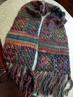 a multicolored crocheted scarf with fringes on top of a table