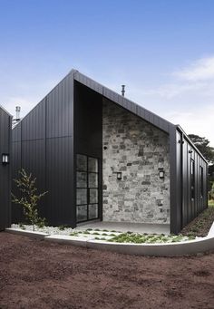 the exterior of a modern house with black siding and stone walls, surrounded by dirt