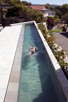 a person swimming in a pool with clear blue water and greenery on the side