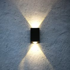 a black square light mounted on the side of a white stucco wall with small holes in it