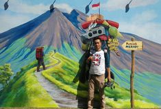 a man is standing in front of a painting with mountains and flags on the wall