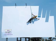 a man on a giant billboard painting the sky with paint rollers and an advertizer