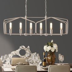 a chandelier hanging over a dining room table with white flowers and wine glasses