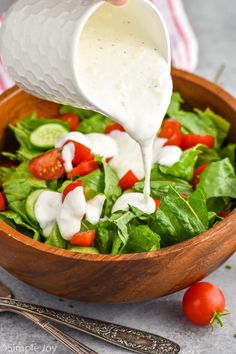 dressing being poured onto a salad in a wooden bowl with tomatoes, cucumbers and lettuce