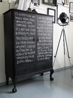 a black cabinet with writing on it in front of a wall full of framed pictures