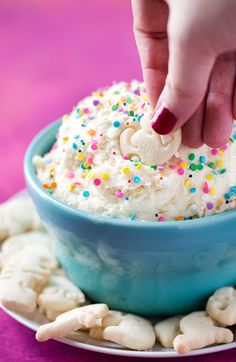 a person dipping marshmallows into a bowl filled with sprinkles