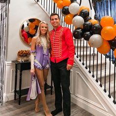 a man and woman standing next to each other in front of a staircase decorated with balloons