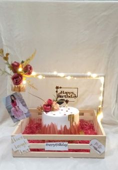 a birthday cake in a wooden box with flowers and pictures on the table next to it