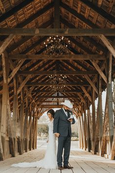 a bride and groom standing under a wooden structure