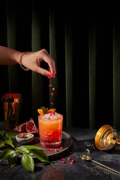 a woman is sprinkling red liquid on a cocktail with garnishes