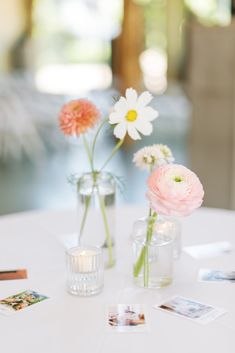 two vases filled with flowers sitting on top of a white table covered in photos