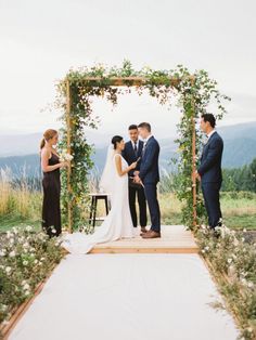 a bride and groom standing under an arch with greenery on it at the end of their wedding ceremony