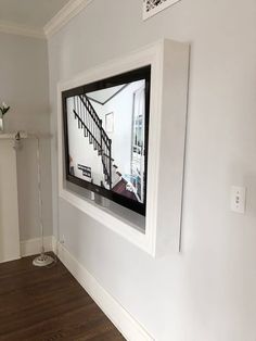 a flat screen tv mounted to the side of a white wall next to a wooden floor