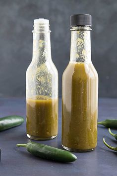 two glass bottles filled with mustard sitting next to green peppers