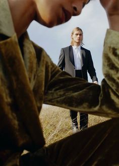 a man in a suit sitting on the ground with his hands to his face while another man stands behind him