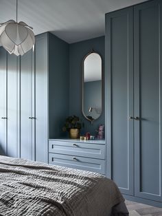 a bedroom with blue painted walls and white furniture, including a large mirror above the bed