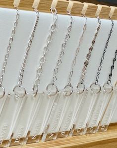 a row of different types of necklaces hanging on a wooden display rack in front of a window