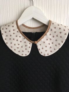 a black and white shirt with brown flowers on the collar is hanging from a hanger