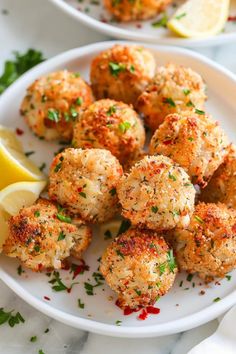 two white plates filled with crab cakes and lemon wedges