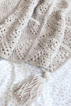 a crocheted blanket laying on top of a bed next to a white pillow