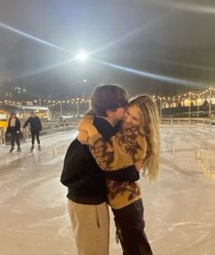 two people hugging each other on an ice rink at night with lights in the background