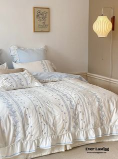 the bed is made with white linens and blue embroidered sheets, along with pillows