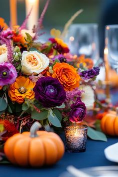 an arrangement of flowers and candles on a table with blue linens, pumpkins and greenery