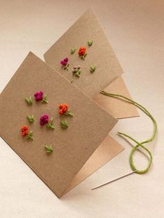 two cards with flowers on them sitting next to green string and thread, one has been made out of brown paper