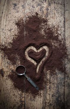 a heart drawn in the sand with a magnifying glass next to it on a wooden surface