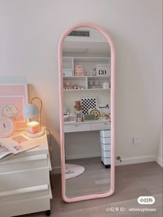 a pink mirror sitting on top of a desk next to a white dresser and drawers