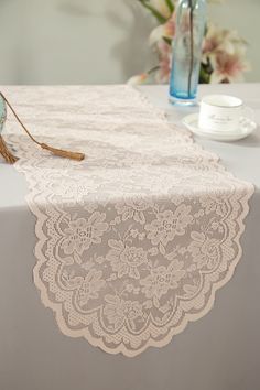 a table topped with a vase filled with flowers and a pink lace runner on top of it